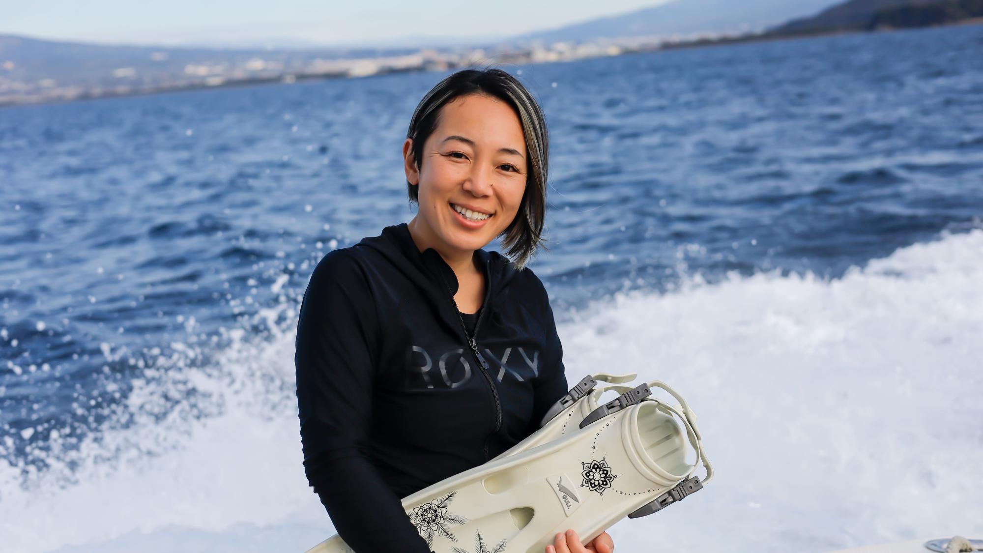 PADI AmbassaDiver Yumi Shirai smiling as she holds her flippers.